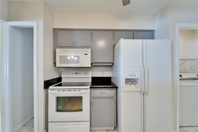 kitchen with dark countertops, white appliances, washer / dryer, and gray cabinetry