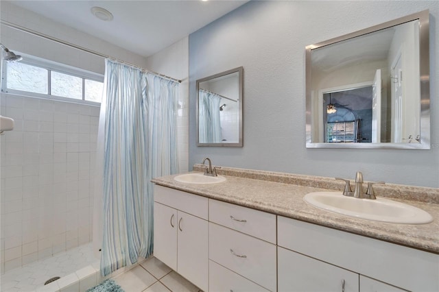 bathroom with double vanity, tiled shower, a sink, and tile patterned floors