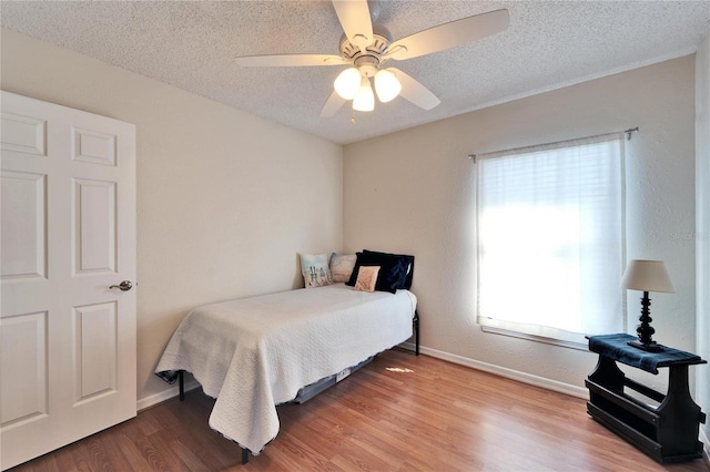 bedroom with ceiling fan, a textured ceiling, baseboards, and wood finished floors