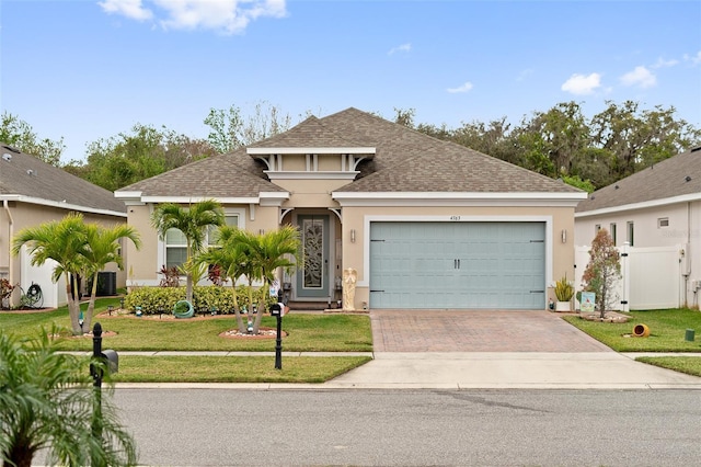 view of front of property featuring a shingled roof, an attached garage, decorative driveway, a front yard, and stucco siding