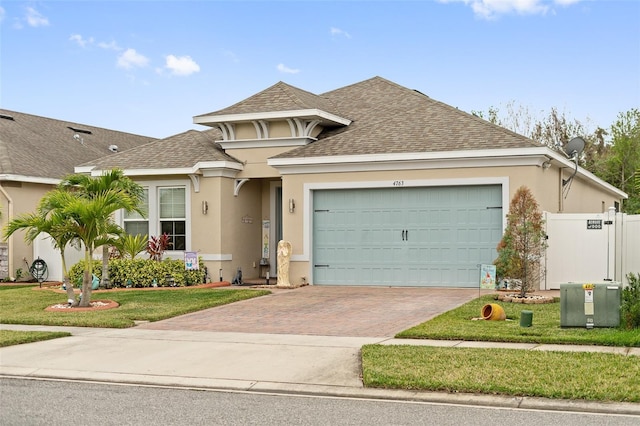 view of front facade featuring a shingled roof, decorative driveway, a front lawn, and stucco siding