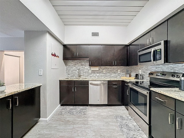 kitchen with light stone counters, stainless steel appliances, tasteful backsplash, visible vents, and a sink