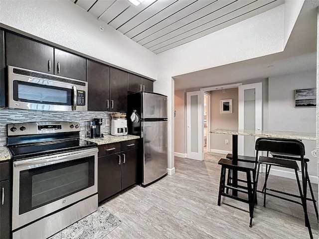 kitchen with dark brown cabinetry, baseboards, stainless steel appliances, and light wood-style floors