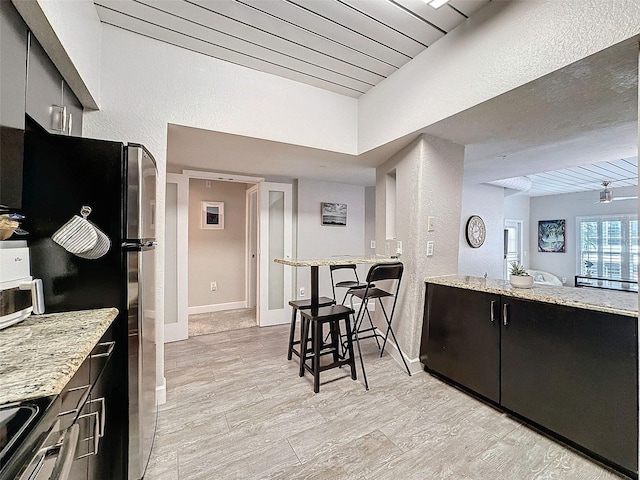 kitchen featuring light stone countertops, baseboards, stainless steel appliances, and dark cabinets