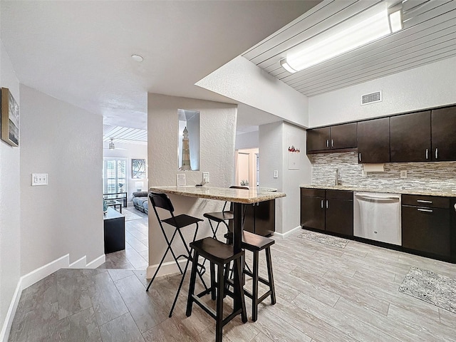 kitchen with a breakfast bar area, dark brown cabinetry, stainless steel dishwasher, light wood finished floors, and tasteful backsplash