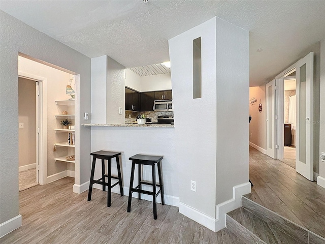 kitchen with a peninsula, light countertops, dark brown cabinets, stainless steel microwave, and a kitchen bar