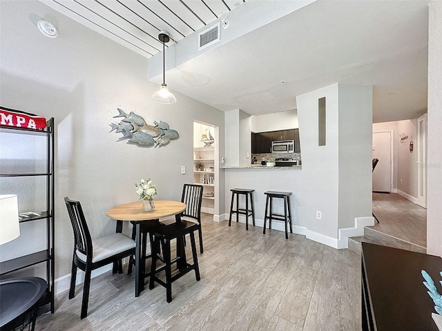 dining room featuring light wood-style floors, built in shelves, and baseboards