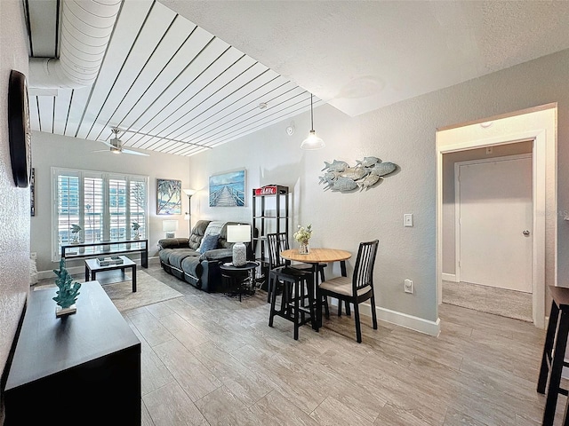 living room featuring a textured wall, light wood-style floors, a ceiling fan, and baseboards