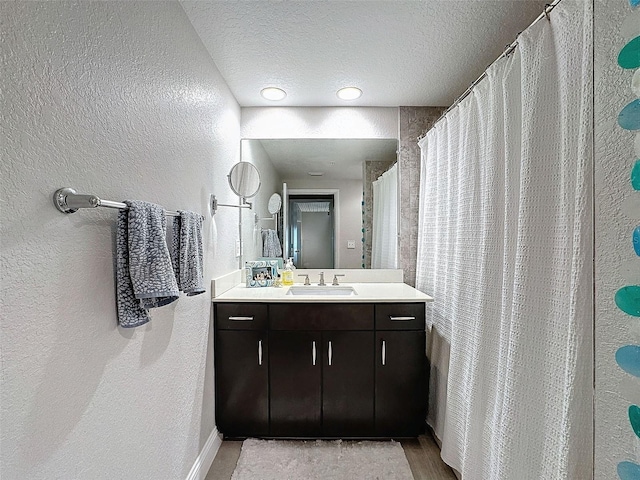 bathroom with a textured ceiling, a textured wall, wood finished floors, and vanity