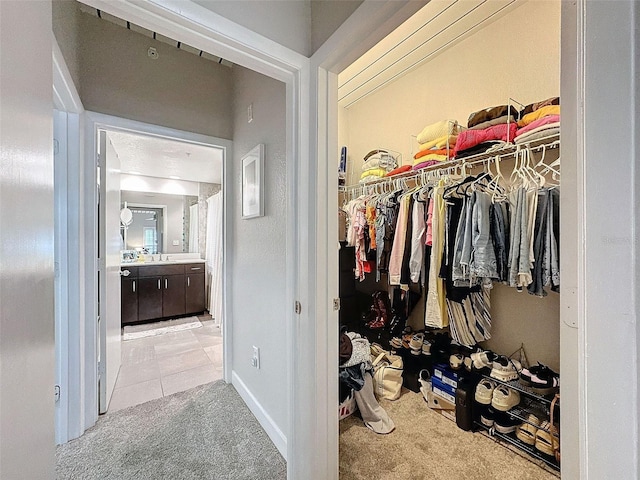 walk in closet with light carpet, light tile patterned floors, and a sink