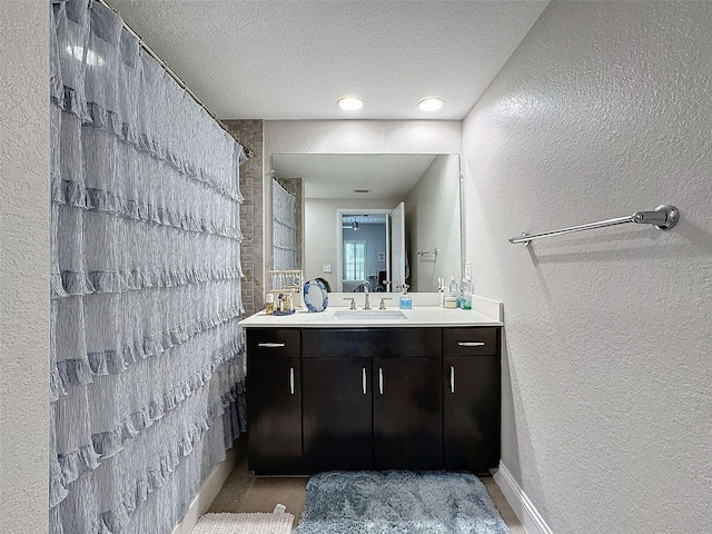 full bathroom featuring a shower with shower curtain, a textured wall, vanity, and a textured ceiling