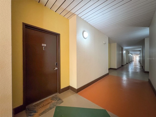 hallway with wood ceiling, finished concrete flooring, and baseboards