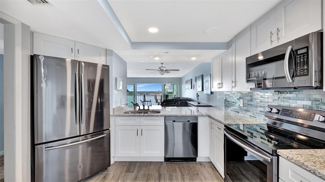 kitchen featuring light stone counters, stainless steel appliances, tasteful backsplash, white cabinets, and a sink