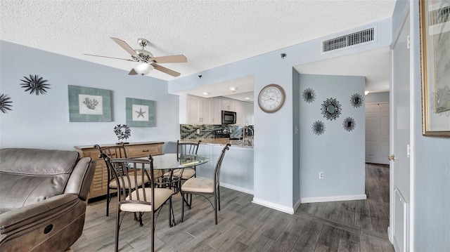 dining space featuring visible vents, a ceiling fan, a textured ceiling, wood finished floors, and baseboards