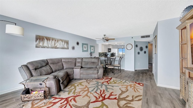 living area featuring visible vents, a textured ceiling, baseboards, and wood finished floors