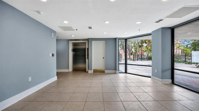 empty room featuring visible vents, baseboards, elevator, expansive windows, and light tile patterned flooring