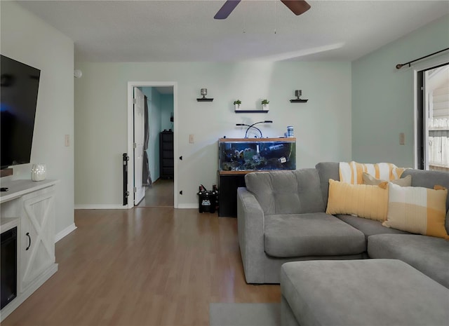 living room featuring a ceiling fan, baseboards, and wood finished floors