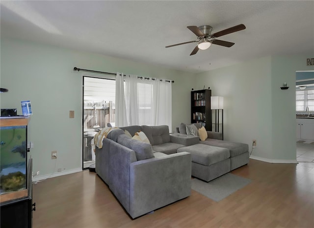 living room with ceiling fan, baseboards, and wood finished floors