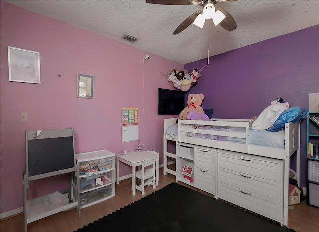 bedroom with a ceiling fan, visible vents, a textured ceiling, and wood finished floors