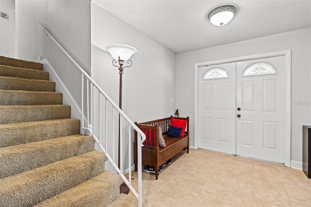 entrance foyer featuring baseboards, stairway, and a textured ceiling