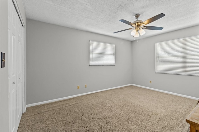 unfurnished bedroom with a textured ceiling, ceiling fan, carpet flooring, baseboards, and a closet