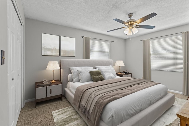 bedroom featuring a closet, light colored carpet, a textured ceiling, and baseboards