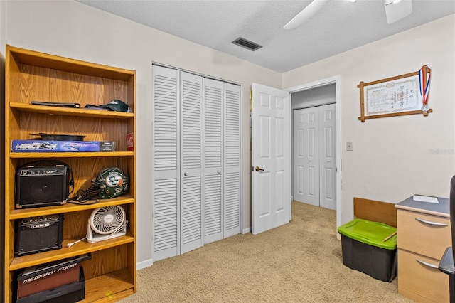 office space with light colored carpet, visible vents, ceiling fan, and a textured ceiling