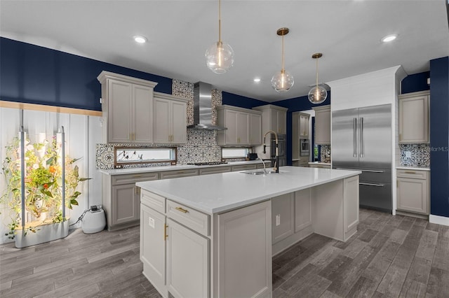 kitchen with decorative light fixtures, light countertops, a sink, wall chimney range hood, and an island with sink