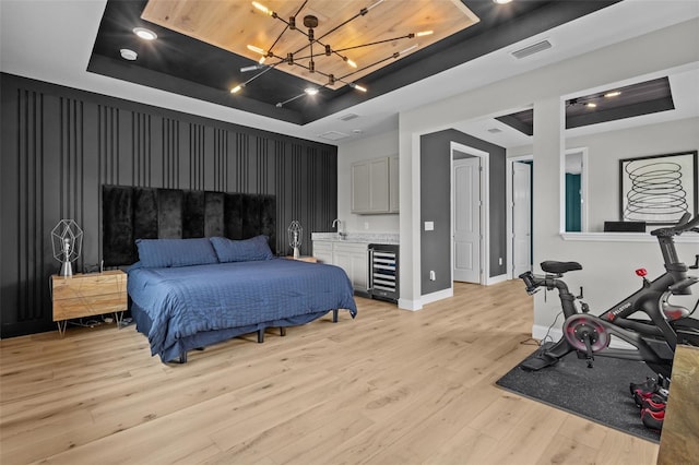 bedroom with light wood-type flooring, a tray ceiling, and beverage cooler