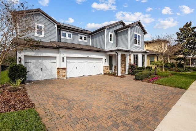 view of front of home with stone siding, decorative driveway, roof mounted solar panels, and an attached garage