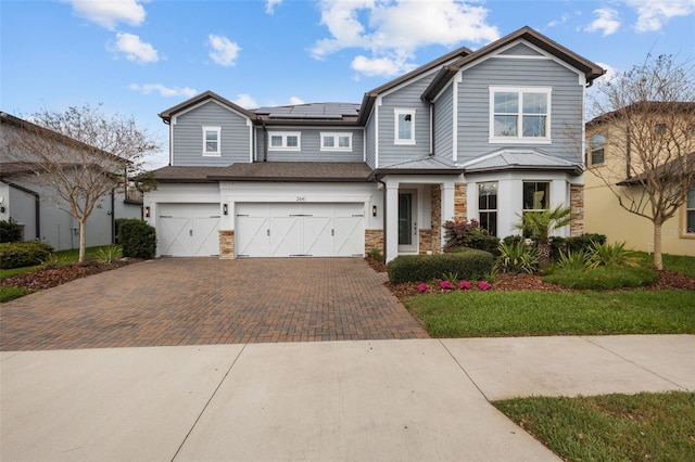 craftsman house with a garage, decorative driveway, stone siding, and solar panels