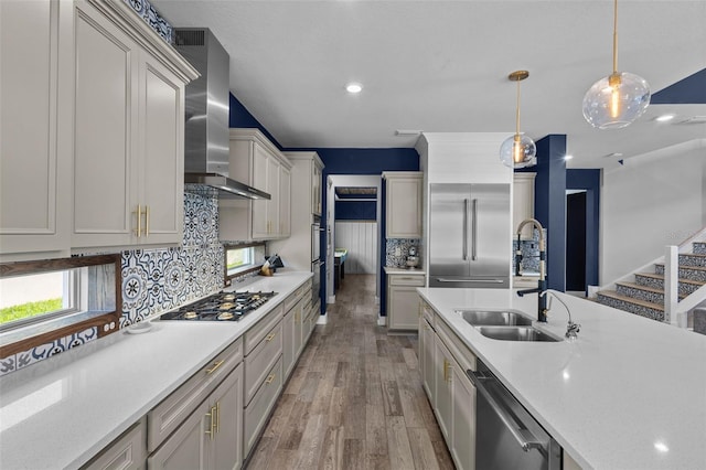 kitchen featuring decorative light fixtures, light wood finished floors, stainless steel appliances, a sink, and wall chimney exhaust hood