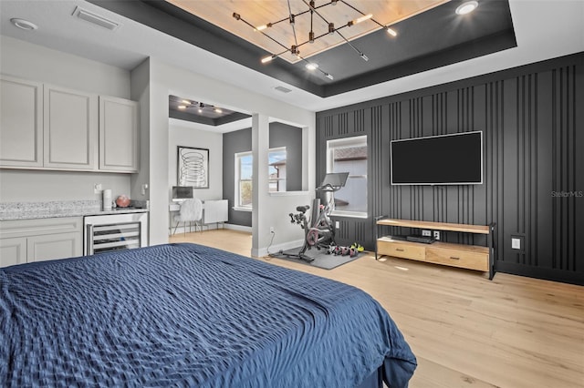 bedroom featuring a tray ceiling, beverage cooler, visible vents, and light wood finished floors