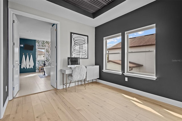 interior space with light wood finished floors, wallpapered walls, baseboards, a raised ceiling, and an accent wall