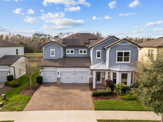 view of front of home featuring decorative driveway, roof mounted solar panels, a standing seam roof, metal roof, and a garage