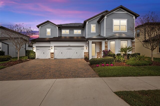 view of front of house with a garage, decorative driveway, stone siding, and solar panels