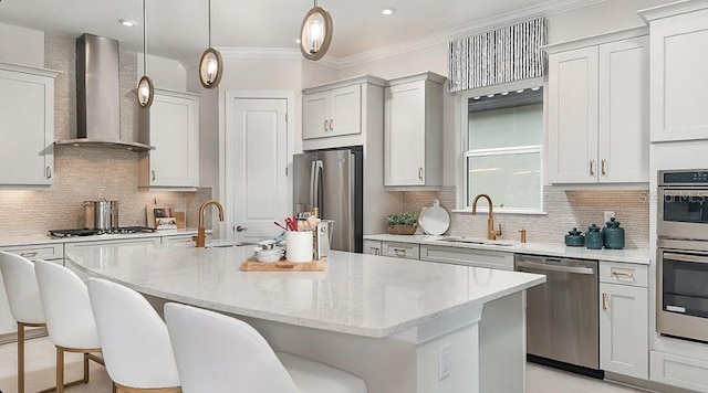 kitchen featuring an island with sink, wall chimney exhaust hood, hanging light fixtures, stainless steel appliances, and a sink