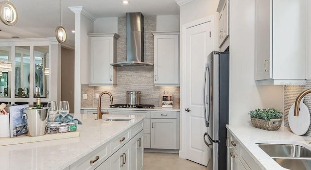 kitchen featuring white cabinets, appliances with stainless steel finishes, light stone counters, wall chimney range hood, and a sink