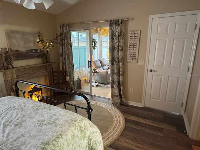 bedroom featuring lofted ceiling, dark wood-style flooring, baseboards, a lit fireplace, and access to outside