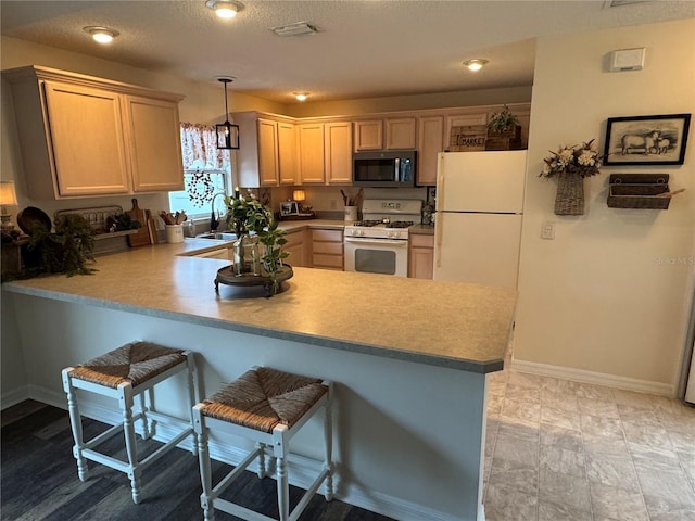 kitchen with white appliances, decorative light fixtures, a peninsula, light countertops, and light brown cabinets