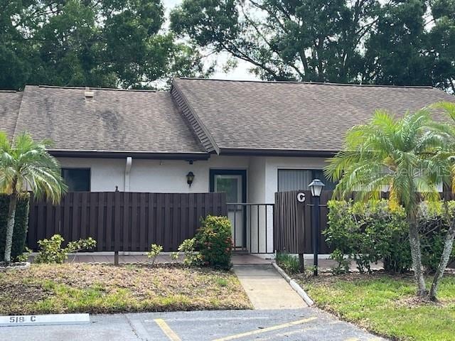 view of front of property with a fenced front yard, uncovered parking, roof with shingles, and stucco siding