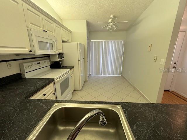 kitchen featuring a textured ceiling, light tile patterned floors, white appliances, a sink, and dark countertops