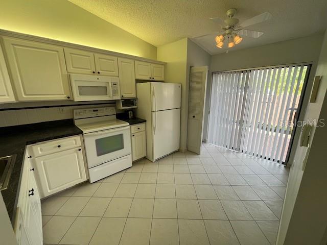 kitchen with lofted ceiling, white appliances, dark countertops, and light tile patterned floors