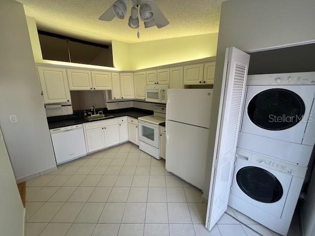 kitchen with white appliances, stacked washer and clothes dryer, dark countertops, vaulted ceiling, and a sink