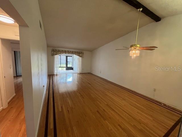 unfurnished living room featuring arched walkways, lofted ceiling with beams, ceiling fan, wood finished floors, and baseboards