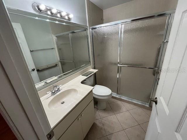 bathroom featuring toilet, vanity, an enclosed shower, and tile patterned floors