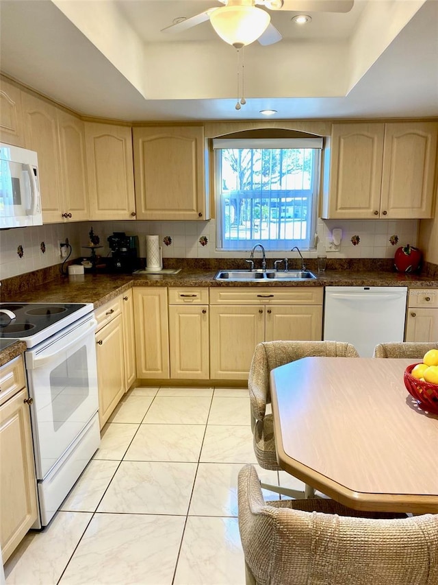 kitchen with white appliances, decorative backsplash, a raised ceiling, light brown cabinets, and a sink