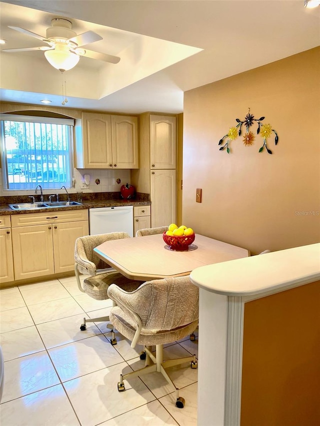 kitchen featuring dark countertops, light brown cabinetry, white dishwasher, and a sink