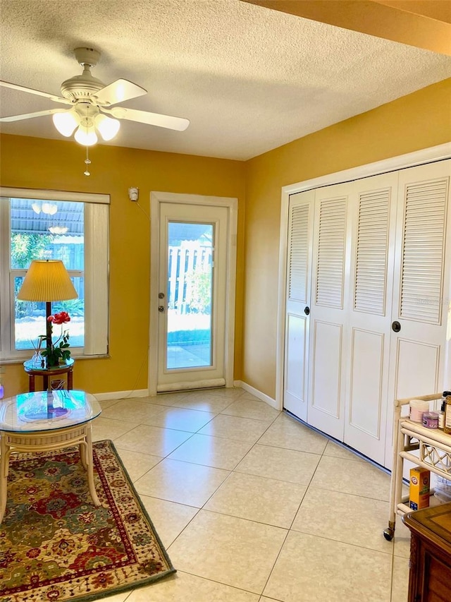 entryway with a textured ceiling, light tile patterned flooring, a ceiling fan, and baseboards