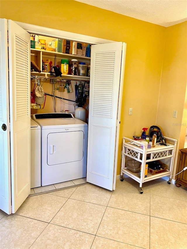 clothes washing area with laundry area, light tile patterned flooring, a textured ceiling, and separate washer and dryer